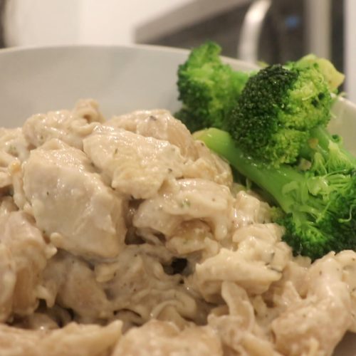 A large white bowl with chicken and creamy pasta with broccoli on the side