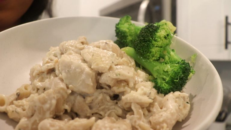 A large white bowl with chicken and creamy pasta with broccoli on the side
